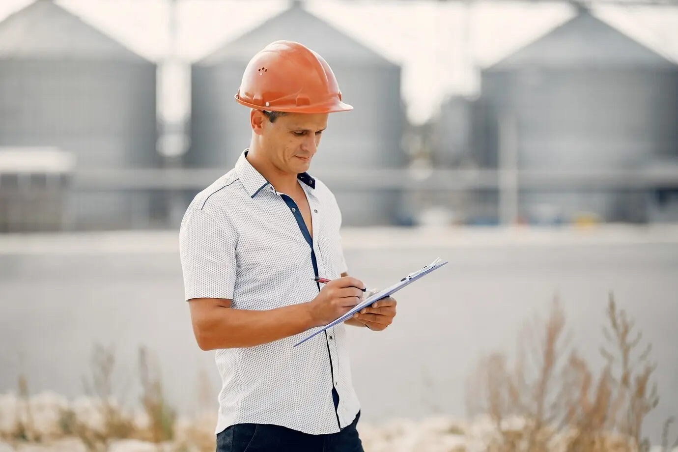 Инженер в каске стоит возле завода.